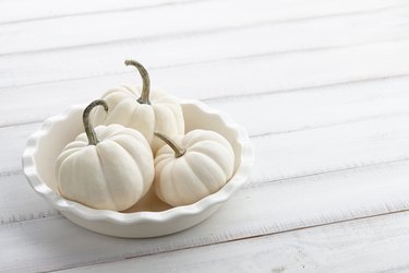 White little pumpkins in a white dish on wooden background